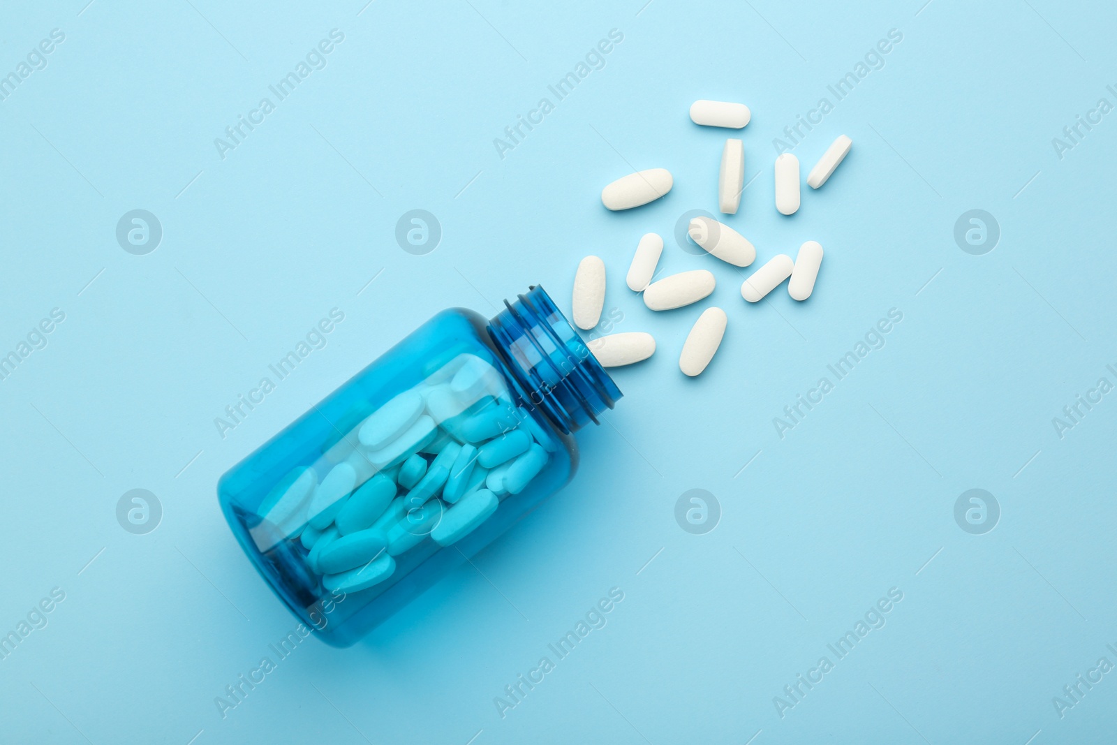 Photo of Vitamin pills and bottle on light blue background, top view