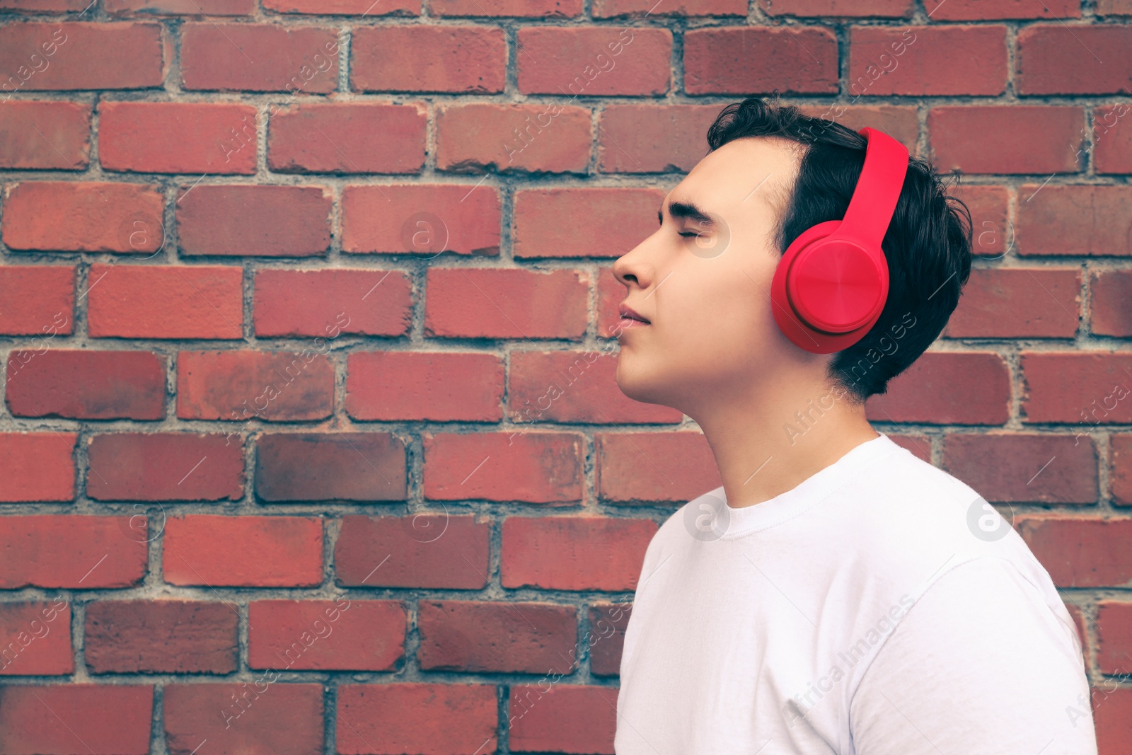 Photo of Handsome young man with headphones near red brick wall. Space for text