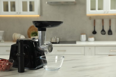 Photo of Electric meat grinder with beef mince on white table in kitchen, space for text