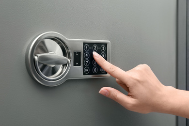 Photo of Woman entering code on keypad of modern safe, closeup