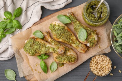 Delicious fried chicken drumsticks with pesto sauce and ingredients on gray table, flat lay