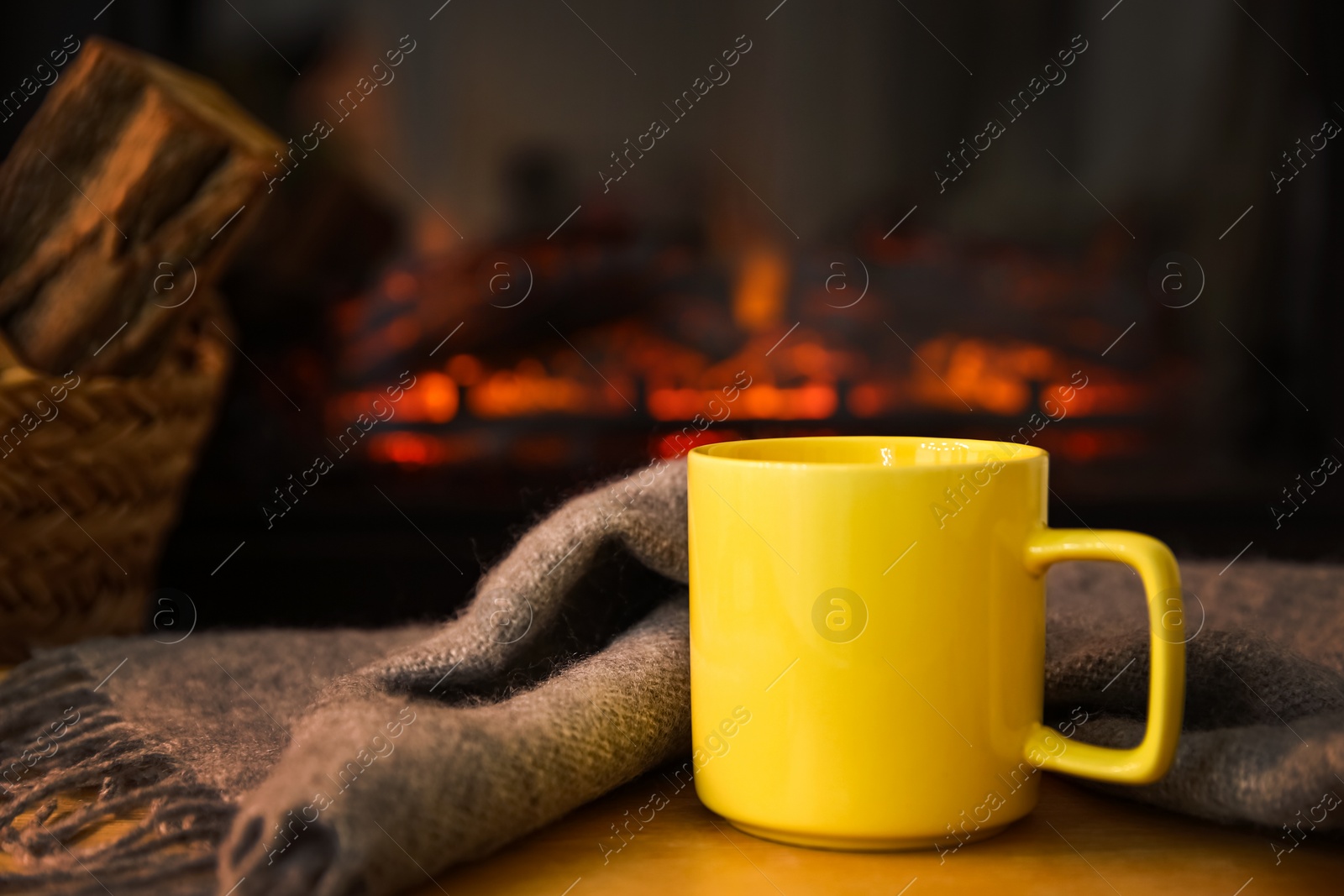 Photo of Cup with hot drink and blanket against fireplace