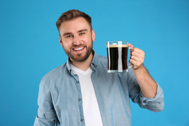 Photo of Handsome man with cold kvass on blue background. Traditional Russian summer drink