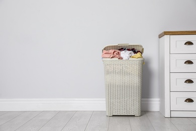 Photo of Plastic laundry basket with dirty clothes near light wall in room. Space for text