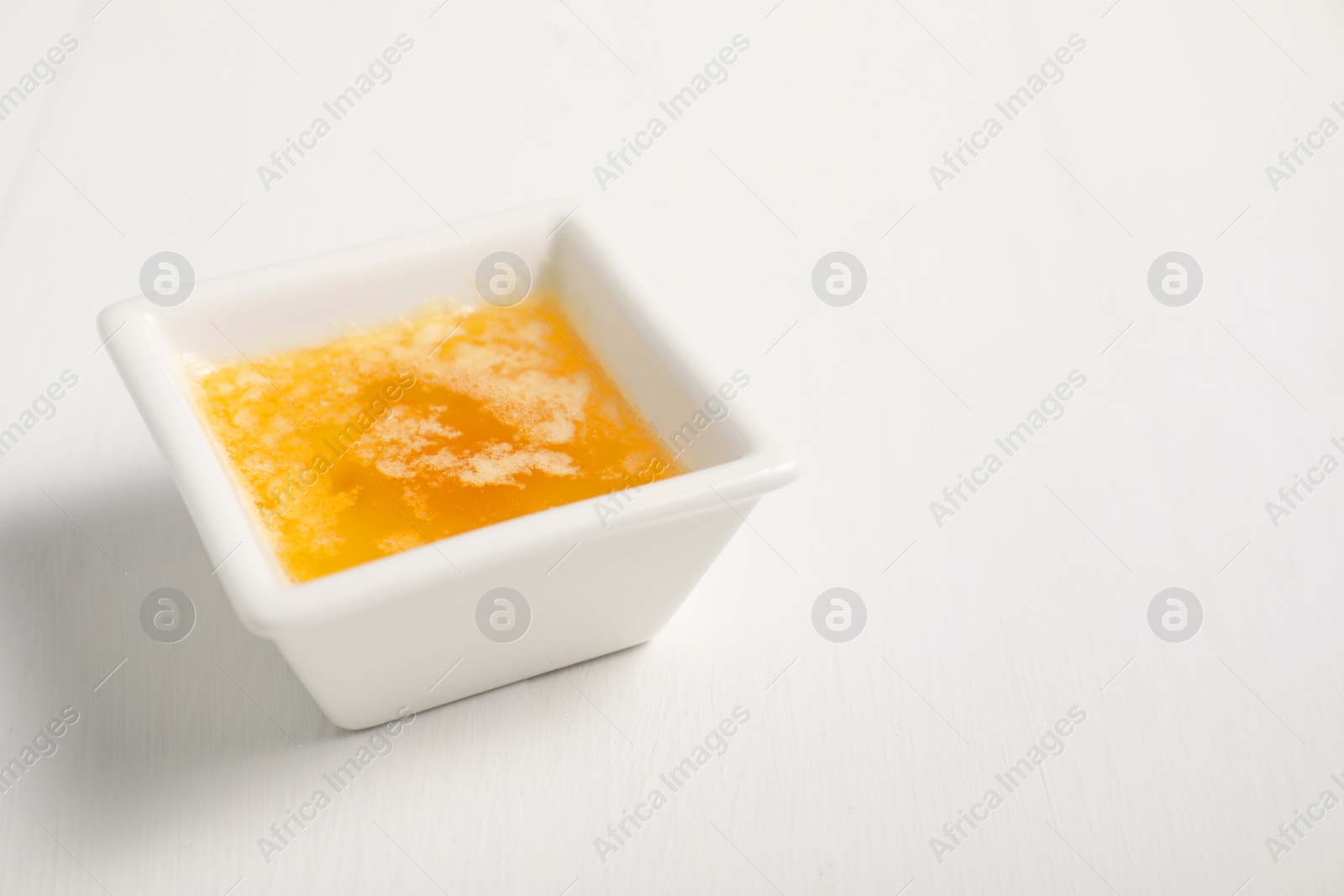 Photo of Melted butter in bowl on white wooden table, closeup. Space for text