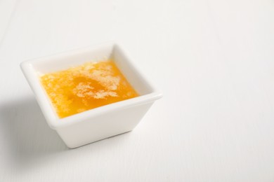 Photo of Melted butter in bowl on white wooden table, closeup. Space for text