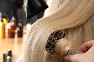 Hairdresser blow drying client's hair in salon, closeup