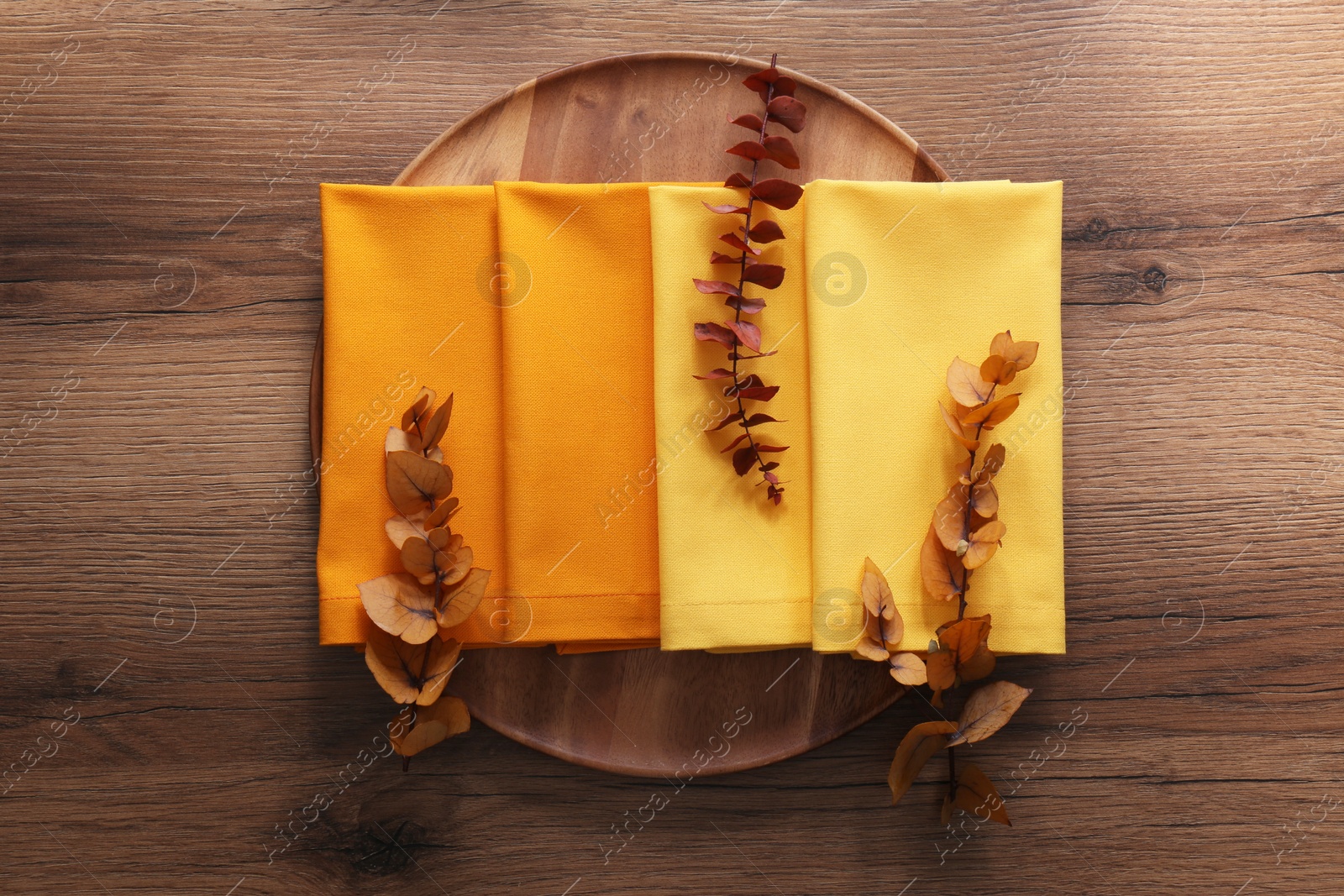 Photo of Tray with different kitchen napkins and decorative dry leaves on wooden table, top view