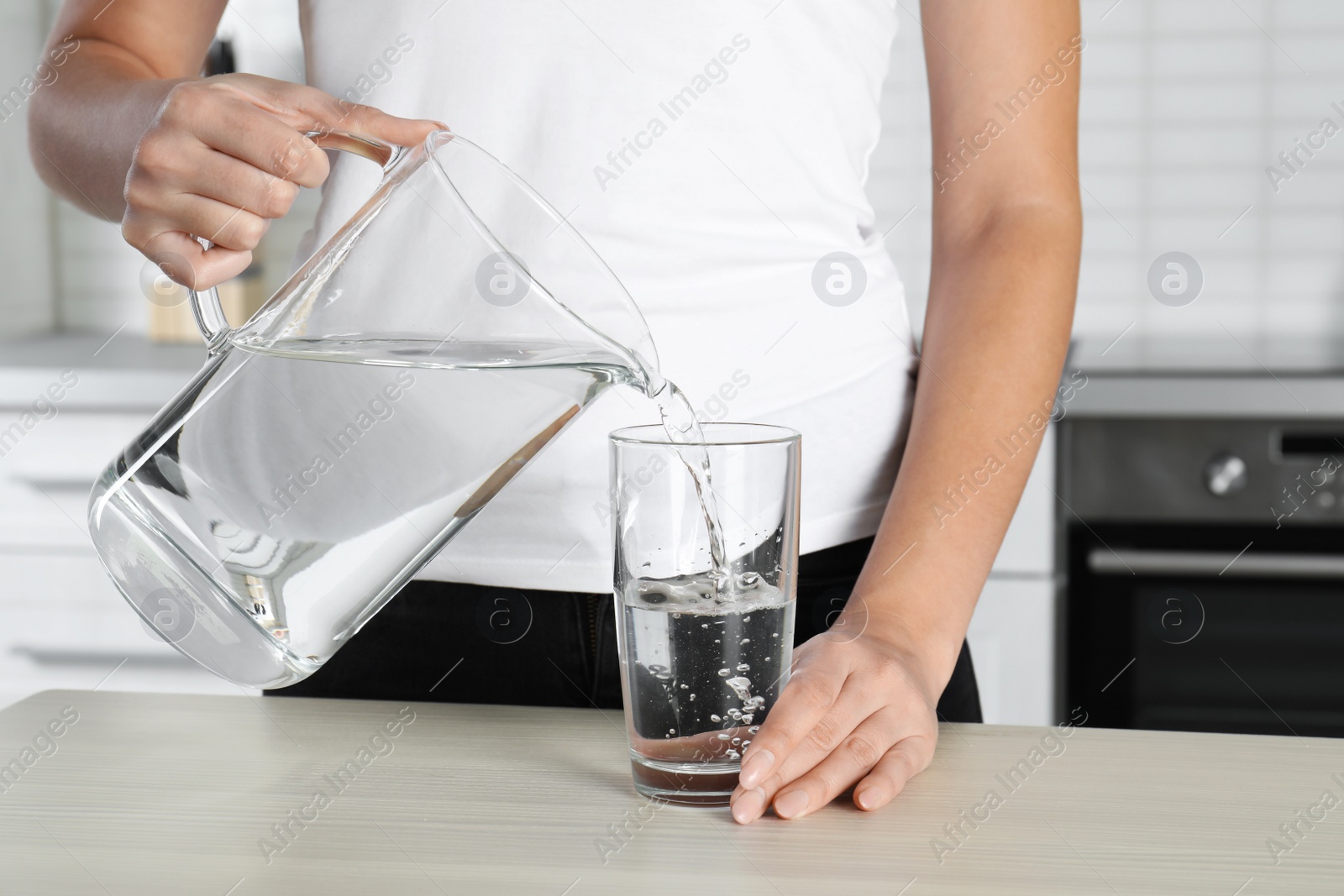 Photo of Woman pouring water into glass at table, closeup