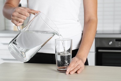 Photo of Woman pouring water into glass at table, closeup