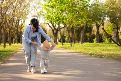 Photo of Mother supporting her baby while he learning to walk outdoors. Space for text