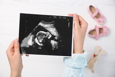 Photo of Woman holding ultrasound photo of baby over table, top view