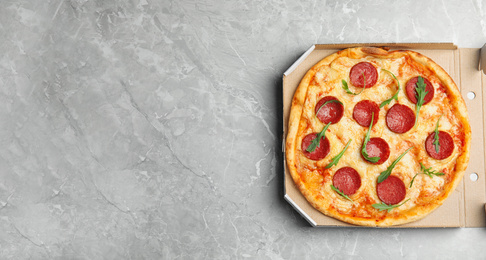 Photo of Tasty pepperoni pizza in cardboard box on light grey marble table, top view. Space for text