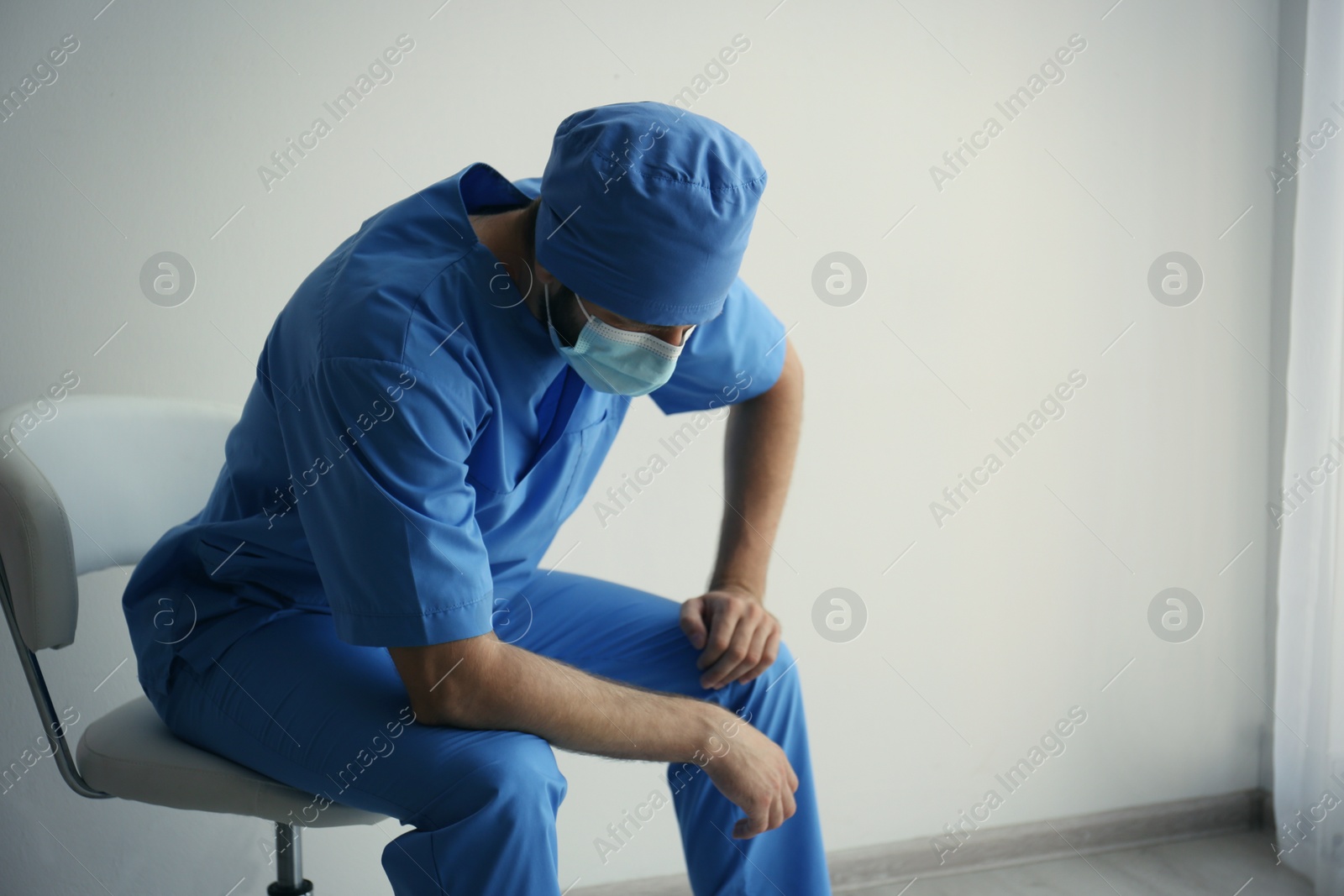 Photo of Exhausted doctor sitting on chair indoors, space for text. Stress of health care workers during COVID-19 pandemic
