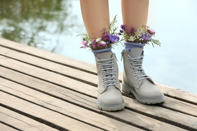 Photo of Woman standing on wooden pier with flowers in socks outdoors, closeup. Space for text