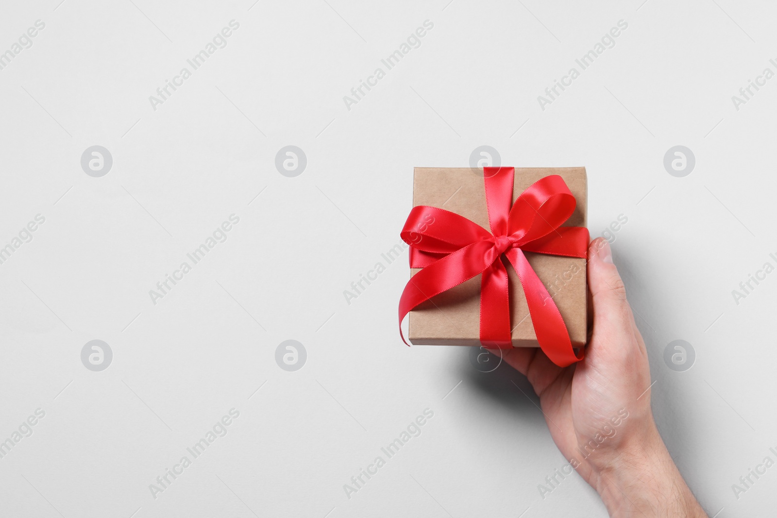 Photo of Man holding gift box with red bow on white background, top view. Space for text