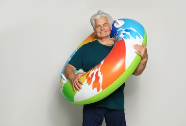 Photo of Funny mature man with bright inflatable ring on light background