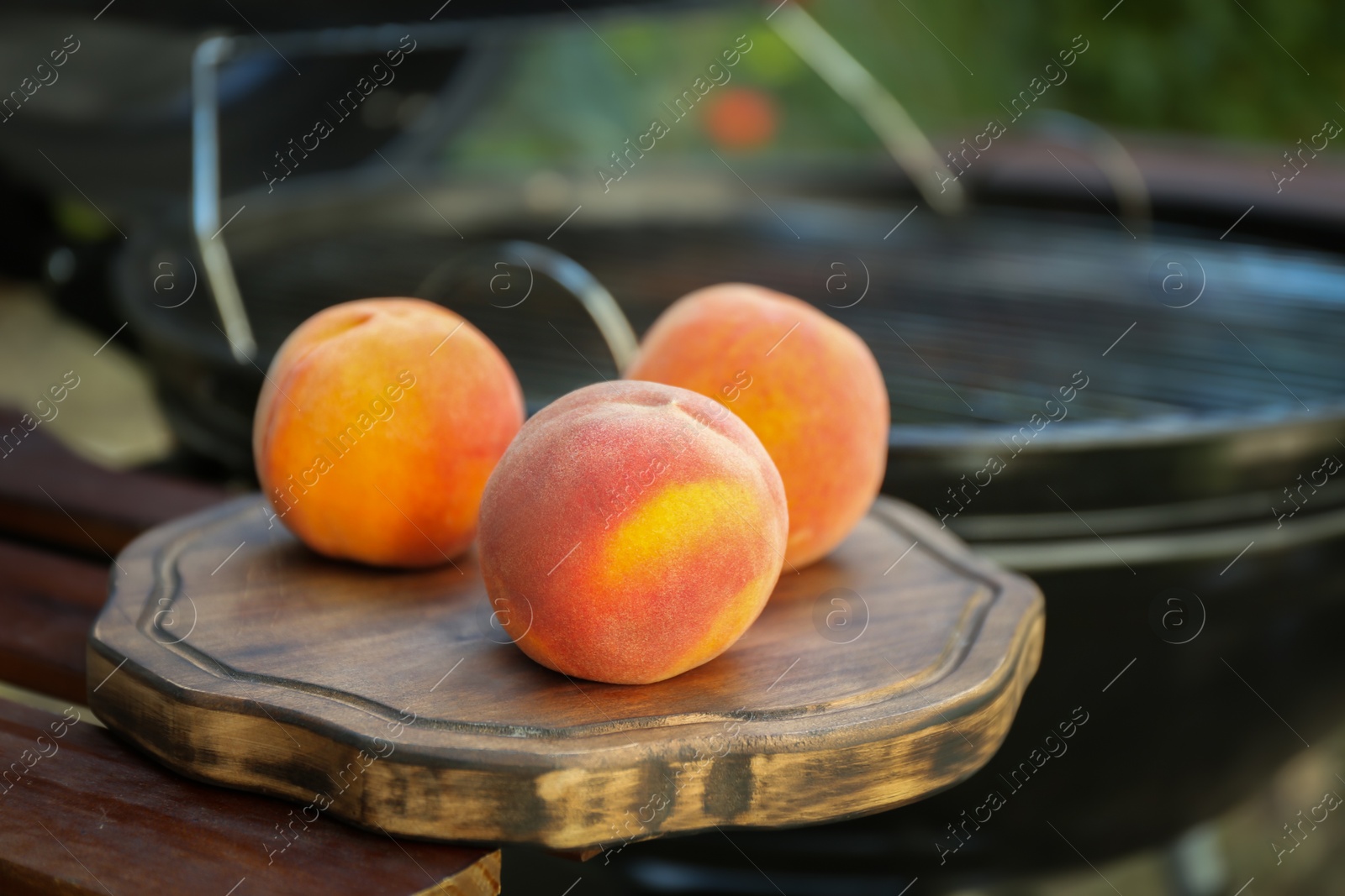 Photo of Fresh peaches on wooden table near modern grill outdoors, closeup