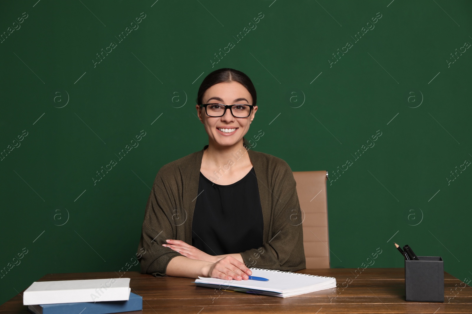 Photo of Portrait of young teacher at table against green background