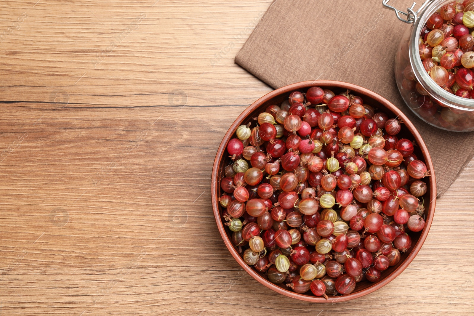 Photo of Bowl and bowl full of ripe gooseberries on wooden table, flat lay. Space for text