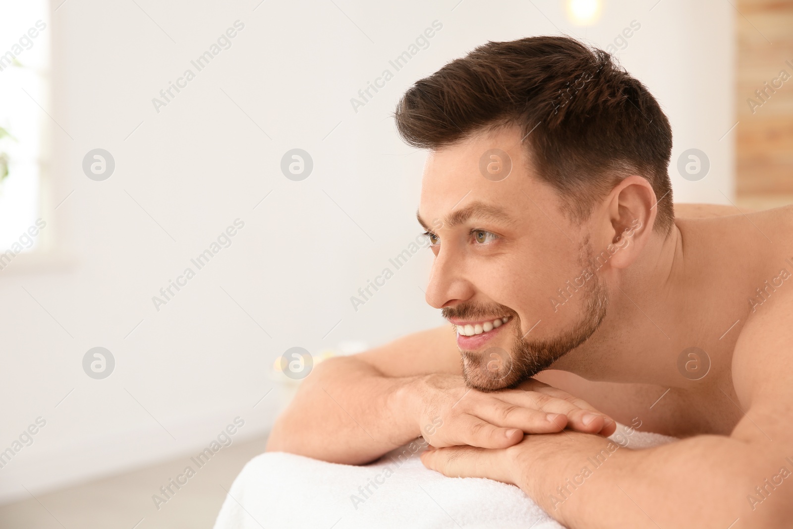 Photo of Handsome man relaxing on massage table in spa salon, space for text