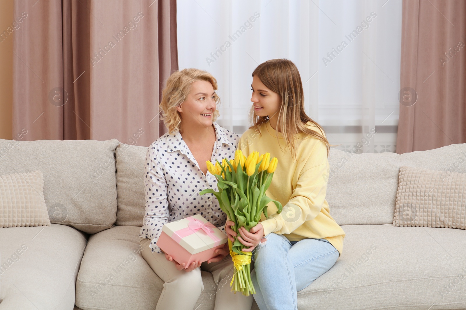 Photo of Young daughter congratulating her mom with flowers and gift at home. Happy Mother's Day