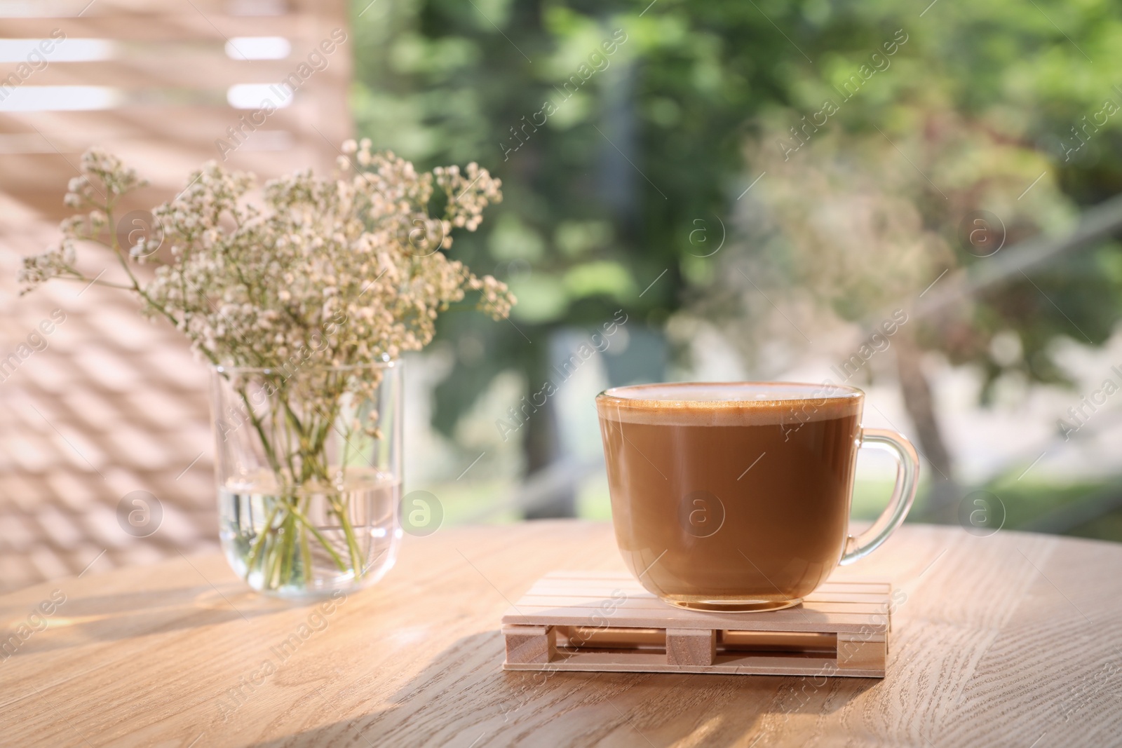 Photo of Cup of delicious morning coffee and flowers on sunlit wooden table
