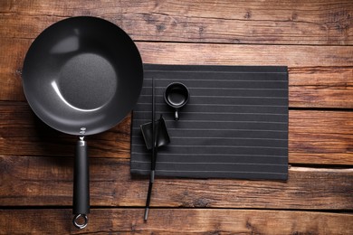 Empty iron wok, sauce bowl and chopsticks on wooden table, flat lay