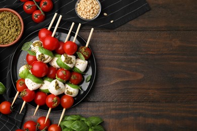 Photo of Caprese skewers with tomatoes, mozzarella balls and basil on wooden table, flat lay. Space for text