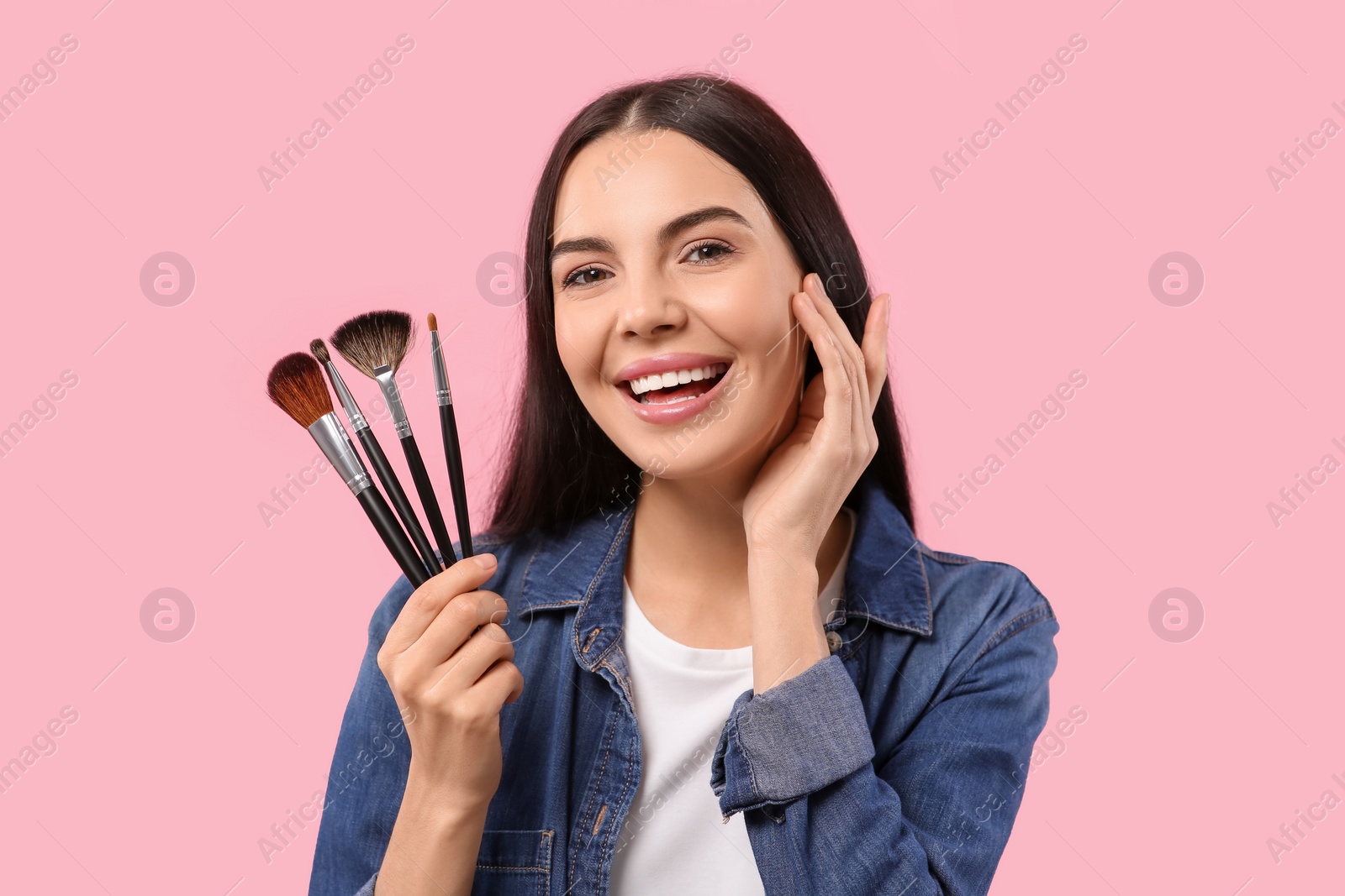 Photo of Happy woman with different makeup brushes on pink background