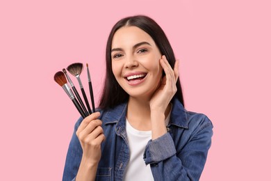 Photo of Happy woman with different makeup brushes on pink background
