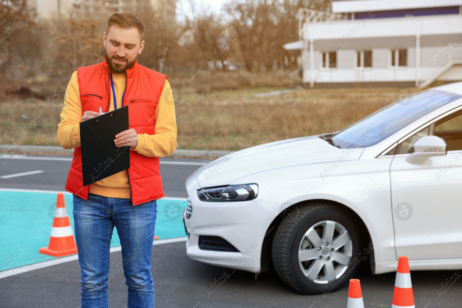 Photo of Instructor with clipboard near car on test track. Driving school