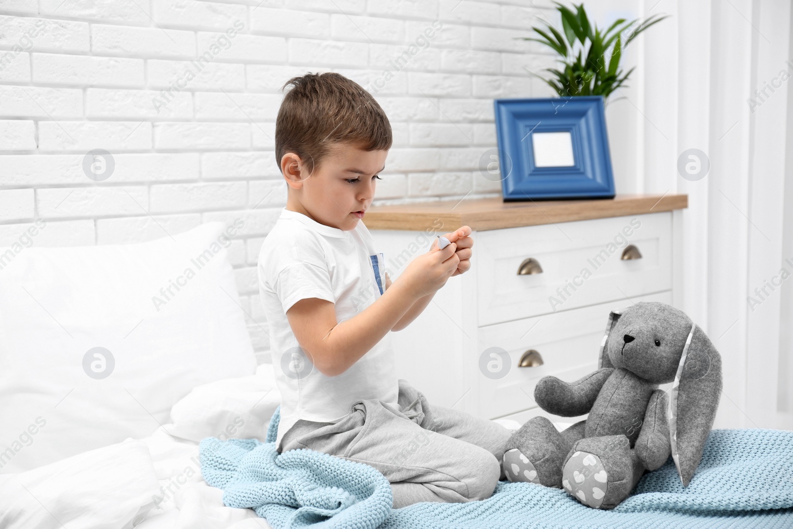 Photo of Cute child playing doctor with stuffed toy on bed in hospital ward