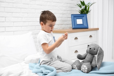 Cute child playing doctor with stuffed toy on bed in hospital ward