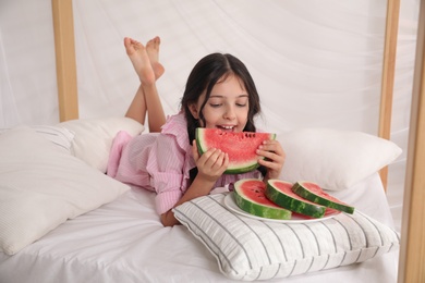 Cute little girl with watermelon on bed at home