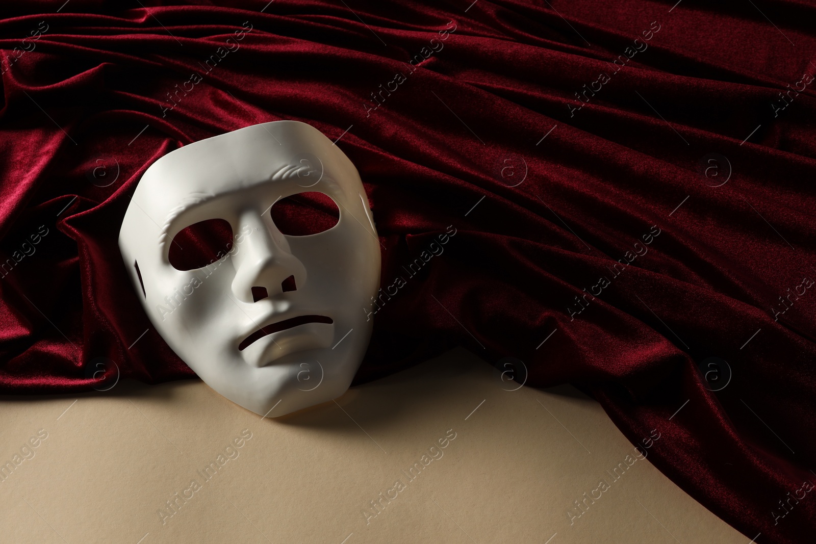 Photo of Theater arts. White mask and red fabric on beige background