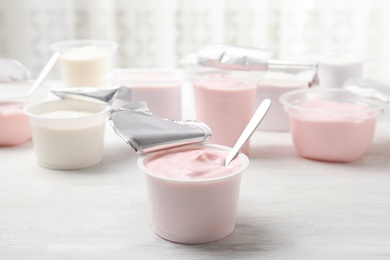 Plastic cup with fresh yogurt and spoon on white wooden table