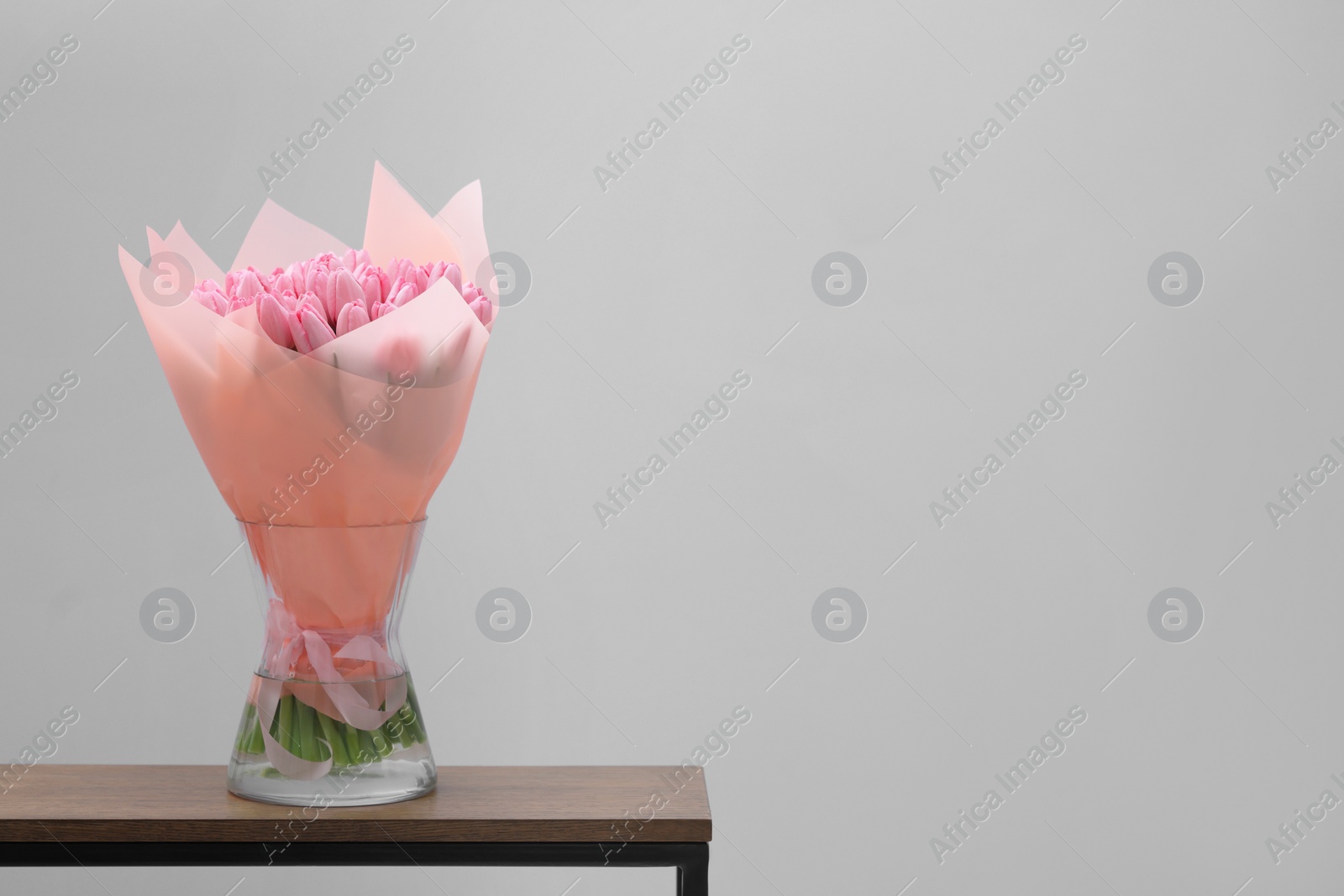 Photo of Bouquet of beautiful pink tulips in vase on wooden table against light grey background, space for text