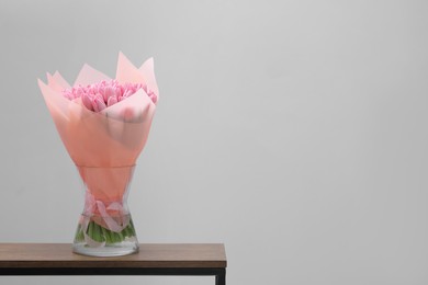Bouquet of beautiful pink tulips in vase on wooden table against light grey background, space for text