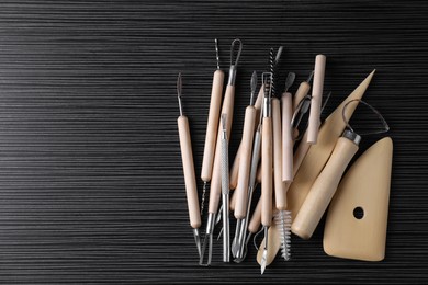 Photo of Clay and set of modeling tools on dark gray wooden table, flat lay. Space for text