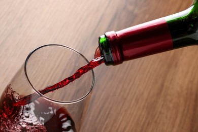 Photo of Pouring tasty red wine in glass at wooden table, closeup