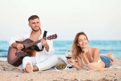 Photo of Young couple with guitar having romantic dinner on beach