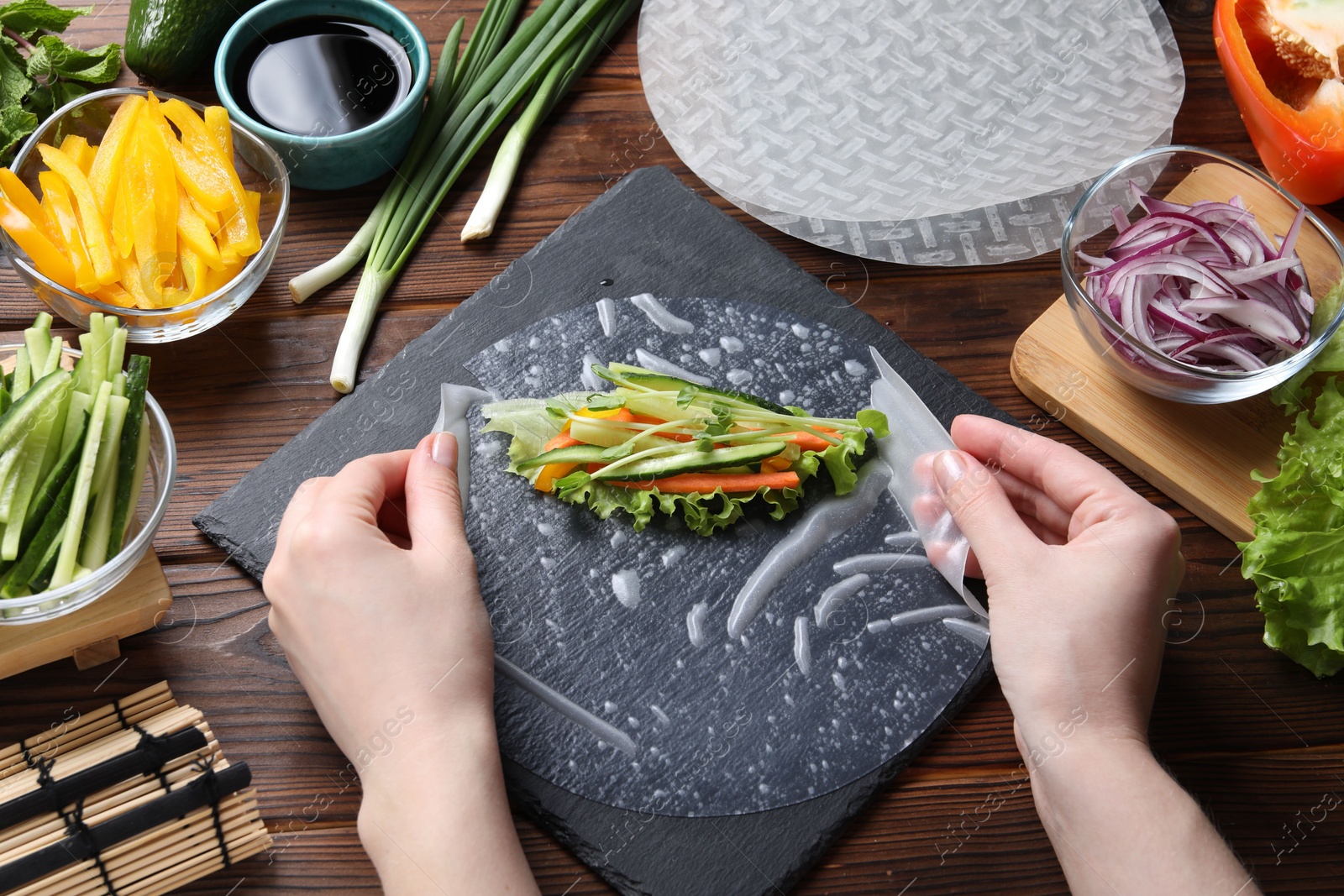 Photo of Woman making spring roll at wooden table with products, closeup