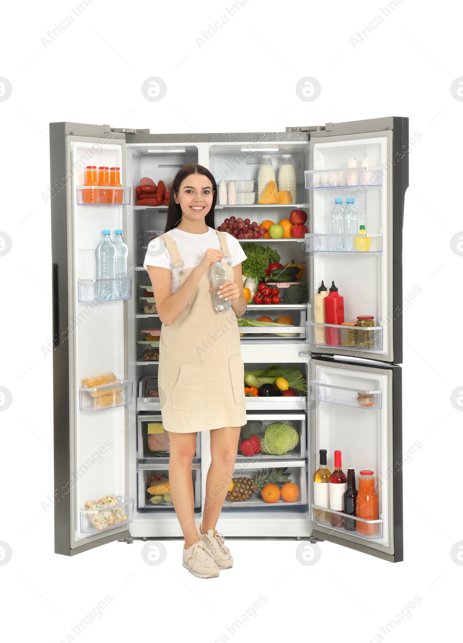 Photo of Young woman with bottle of water near open refrigerator on white background