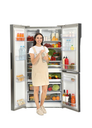 Photo of Young woman with bottle of water near open refrigerator on white background