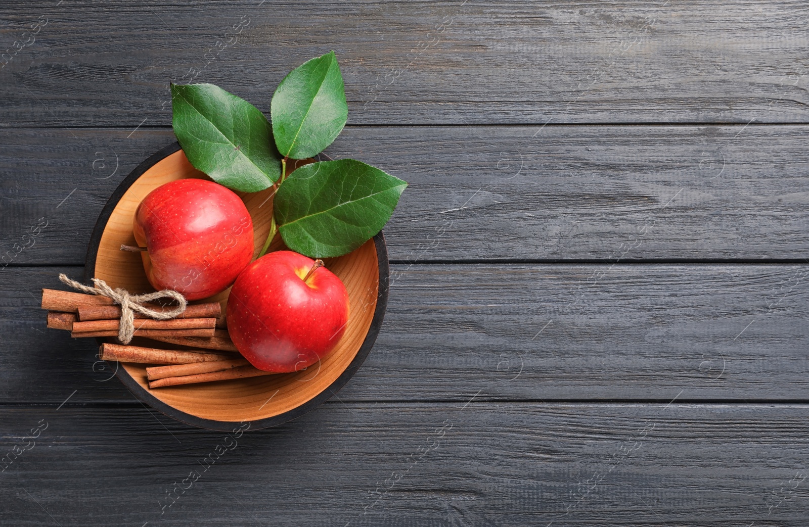 Photo of Fresh apples and cinnamon sticks in bowl on wooden table, top view