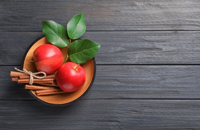 Photo of Fresh apples and cinnamon sticks in bowl on wooden table, top view