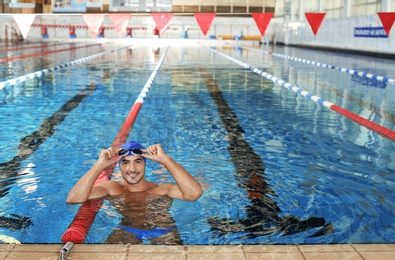 Photo of Young athletic man wearing cap and goggles in swimming pool