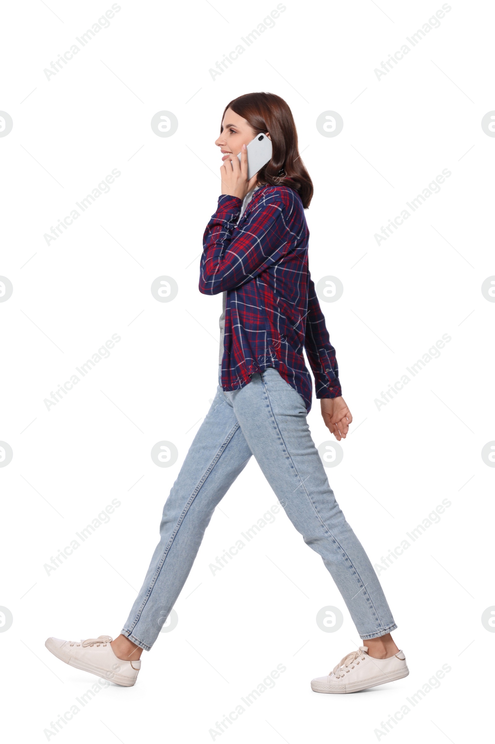 Photo of Happy young woman in casual outfit talking on smartphone while walking against white background