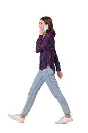 Happy young woman in casual outfit talking on smartphone while walking against white background